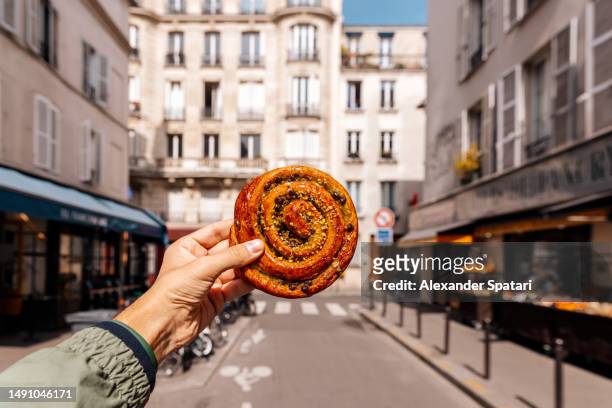 man holding fresh french pastry pain aux raisins on a street in paris, france - paris france stock pictures, royalty-free photos & images