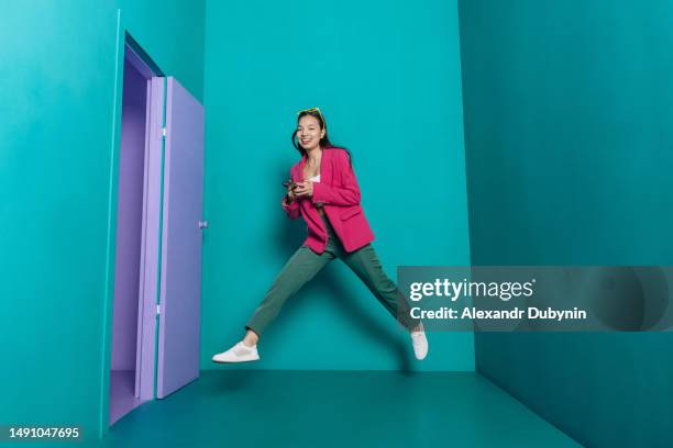 happy asian woman jumping in color room holding smartphone - phone mid air stock pictures, royalty-free photos & images
