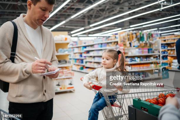 dad with a shopping list, daughter in a grocery cart - family shopping list stock pictures, royalty-free photos & images