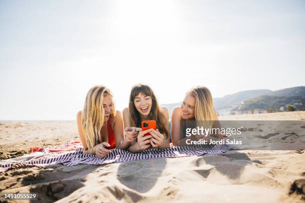 three women on the beach using a phone - beach sunbathing spain fotografías e imágenes de stock