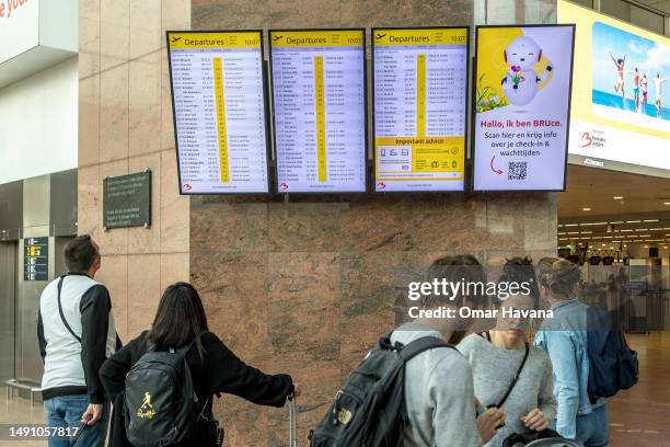 Passengers verify the check-in desk for their flights on the departure terminal's flight screens inside the Belgian capital's airport on May 17, 2023...