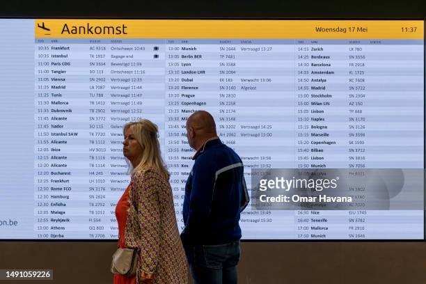Couple walk past the flight arrival information screen in the arrivals terminal of the Belgian capital's airport on May 17, 2023 in Brussels,...