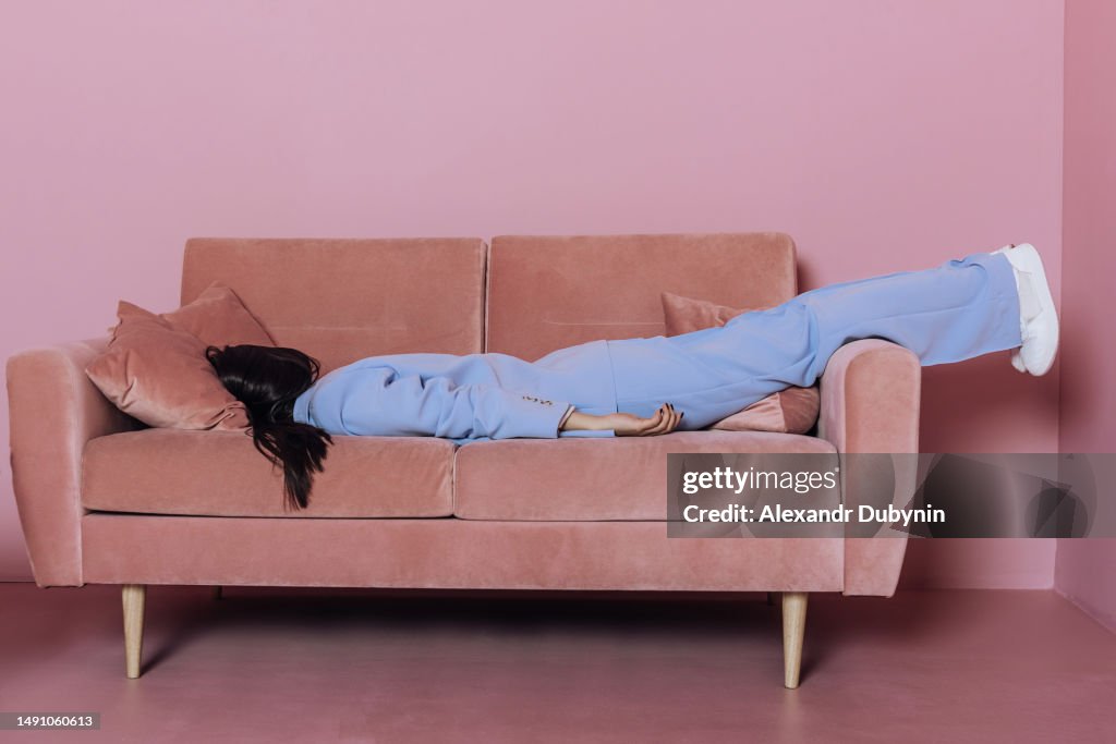 Creative portrait of a woman lying in a blue suit on a pink sofa. Fashion concept.