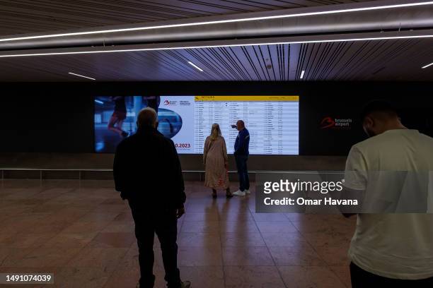 People await the arrival of family and friends in front of the flight information screen in the arrivals terminal of the airport in the Belgian...