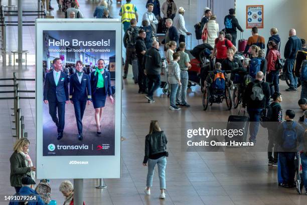 Passengers walk towards their boarding gates and check-in counters as a Transavia airline advertisement welcomes them to Brussels in the departure...