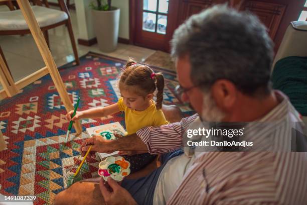 grandfather and granddaughter having fun and painting at home - kleindochter stockfoto's en -beelden