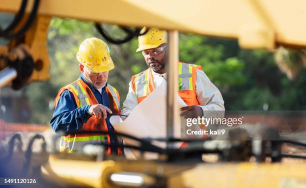 two multiracial construction workers reviewing blueprint - road construction stock pictures, royalty-free photos & images