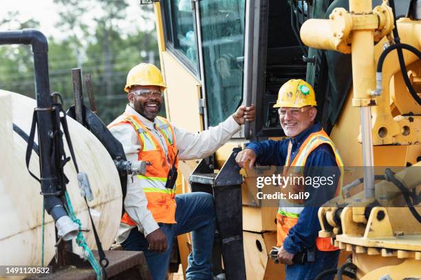 multiracial construction workers at job site by grader - wegenbouw stockfoto's en -beelden