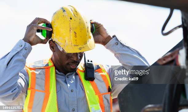 man at construction site putting on ear protectors - ear defenders stock pictures, royalty-free photos & images