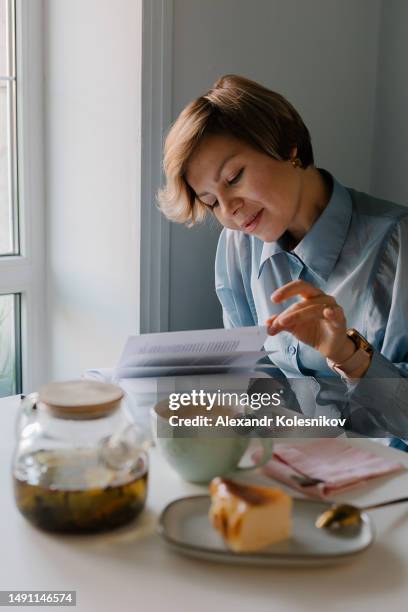 glass teapot with green healthy tea, a cheesecake dessert and a mug. young woman reading a book is sitting in cafe - cheesecake white stock pictures, royalty-free photos & images