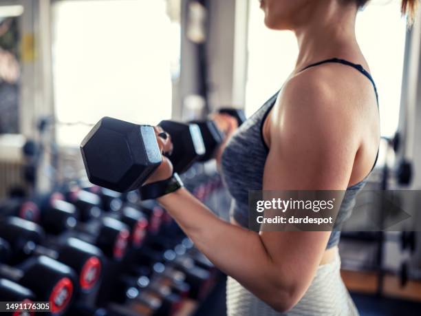 mujer joven levantando pesas en el gimnasio - levantamiento de pesas fotografías e imágenes de stock