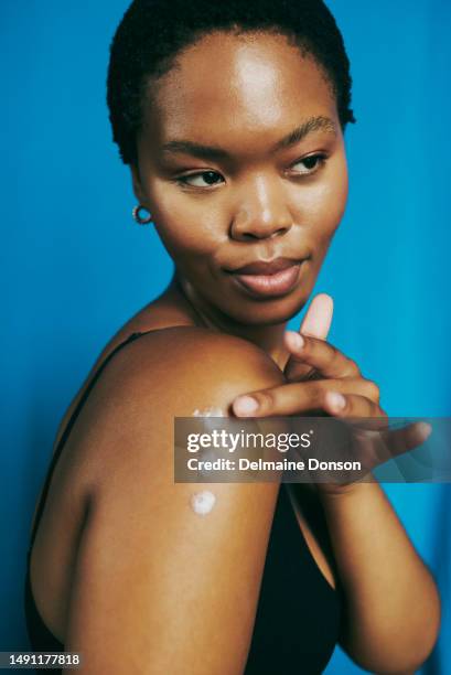 fresh faced beauty. beautiful young black woman looking over her shoulder whilst applying body lotion. stock photo - dark skin tone stock pictures, royalty-free photos & images