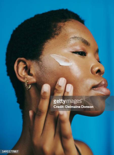 headshot of a beautiful black woman, looking down and thinking  as she applies moisturizer to her face with her head tilted backwards, stock photo - black makeup stockfoto's en -beelden