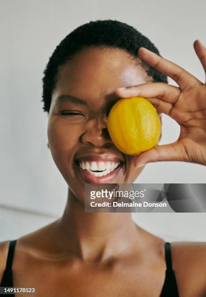 happy young black woman making facial expressions while laughing with her eyes closed and holding a lemon in her hand, stock photo - face close up bildbanksfoton och bilder