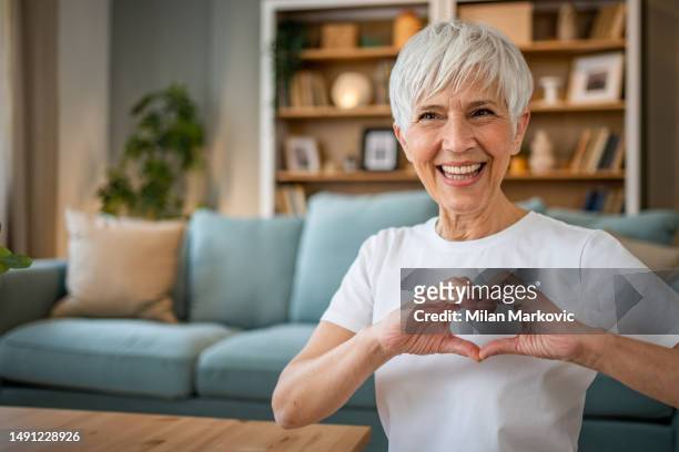 happy elderly woman making a heart sign with her hands - hand with hart stockfoto's en -beelden