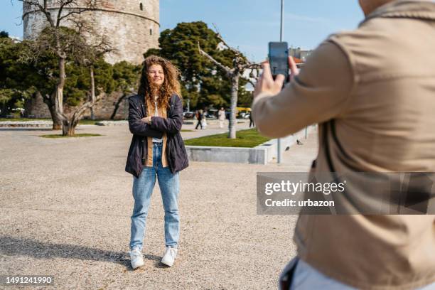 freund macht fotos von seiner freundin vor dem weißen turm in thessaloniki - greek woman stock-fotos und bilder