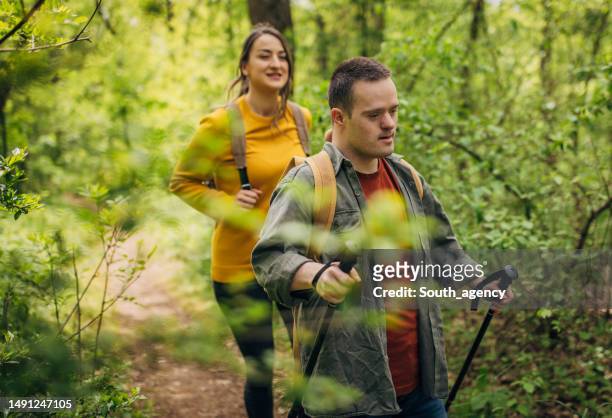 two friends, a young woman and man with down syndrom, hiking together in the forest - disabilitycollection stock pictures, royalty-free photos & images