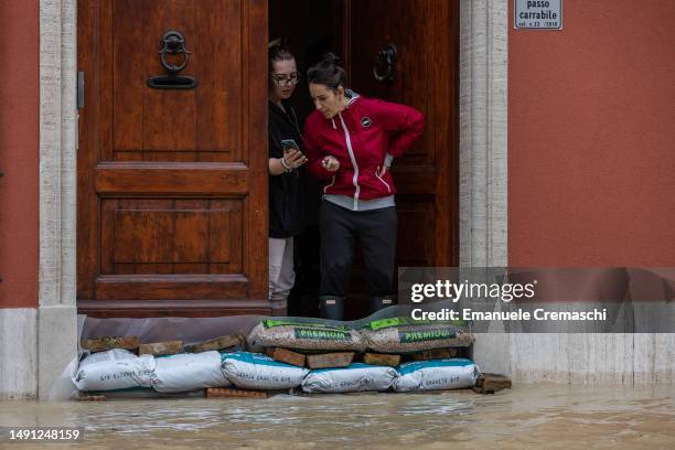 Two women stand on the doorsteps of their house, behind a pile of sandbags on May 18, 2023 in Lugo, Italy. Nine people have died and thousands have...