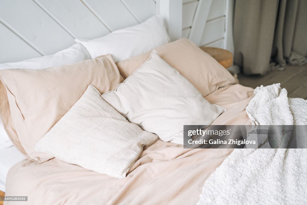 Beige cotton bed linen pillows blanket on wooden eco style bed in bedroom at home