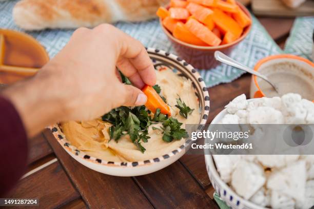 hand taking hummus with carrot at table - spoon in hand ストックフォトと画像