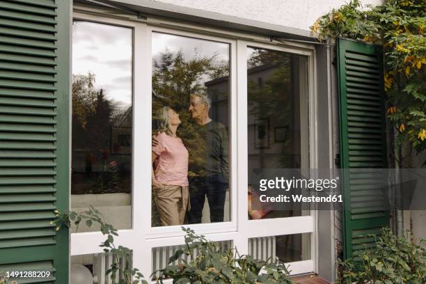 senior couple behind windowpane of their home - best ager paar garten stock-fotos und bilder