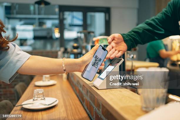 here is a close-up photo taken in a restaurant, showing a woman holding her smartphone while interacting with a restaurant staff member to make a payment. - qr code food and drink stock pictures, royalty-free photos & images