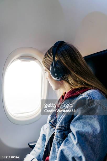 woman wearing headphones looking out of window sitting in airplane - woman airplane headphones bildbanksfoton och bilder