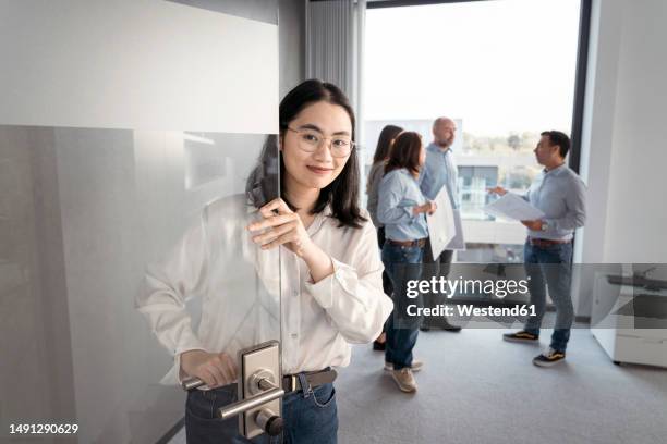 portrait of young businesswoman opening door with colleagues in background in office - open day 5 stock pictures, royalty-free photos & images