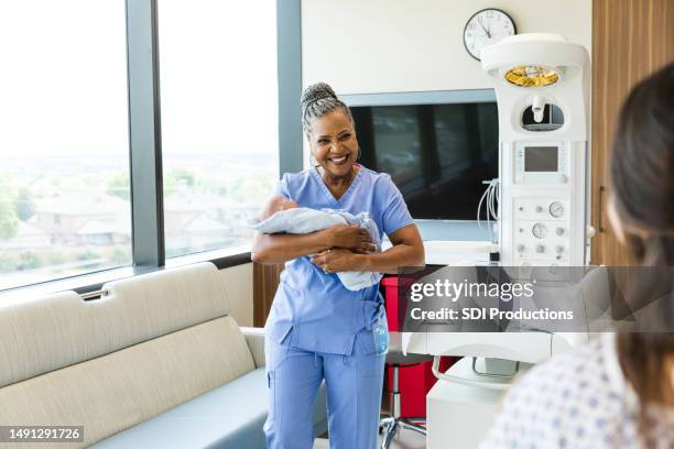 una doctora sonriente lleva al bebé a una nueva madre irreconocible - comadrona fotografías e imágenes de stock