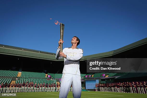 Andy Murray of Great Britain holds the Olympic Torch aloft on Centre Court at the All England Lawn Tennis and Croquet Club in Wimbledon on July 23,...