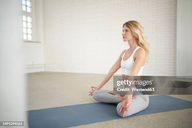Young slim woman with blonde hair sitting on the yoga mat in split and  training her stretching - using auxiliary stand under the feet Stock Photo  - Alamy