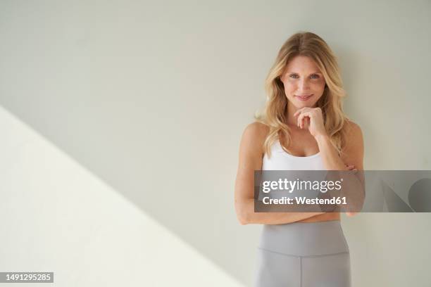 smiling woman with hand on chin in front of wall - three quarter length stock pictures, royalty-free photos & images