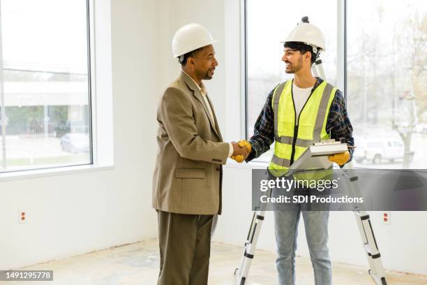 young adult foreman shakes hands with the business man to welcome him to the job site - contractors clipboard stock pictures, royalty-free photos & images