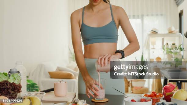 young asian athletic woman using blender and pouring smoothie to glass at home. healthy food. - smoothie home stock pictures, royalty-free photos & images
