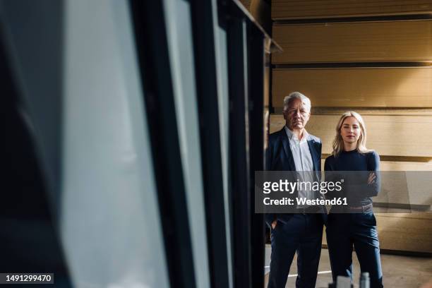 businessman with hands in pockets standing by colleague in factory - successor stockfoto's en -beelden