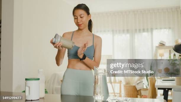 young asian athletic woman preparing protein shake at home. diet and healthy food. - protein shaker stock pictures, royalty-free photos & images