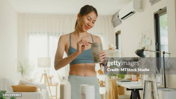 young asian athletic woman preparing protein shake at home. diet and healthy food. - asian female bodybuilder stock pictures, royalty-free photos & images