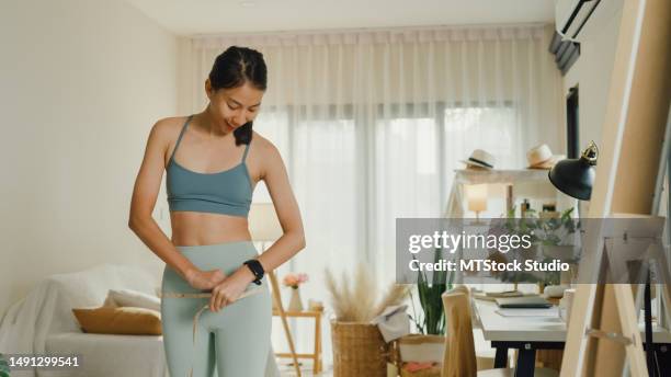 young asian athletic woman with a tape measure body perfect slim weight loss in front of a mirror in living room at home. diet and healthy weight loss. - fat loss training stock pictures, royalty-free photos & images