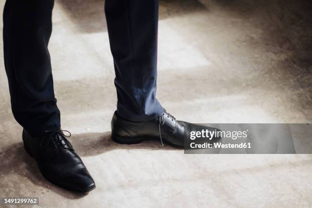 legs of businessman wearing black formal shoes standing in factory - eleganter schuh stock-fotos und bilder