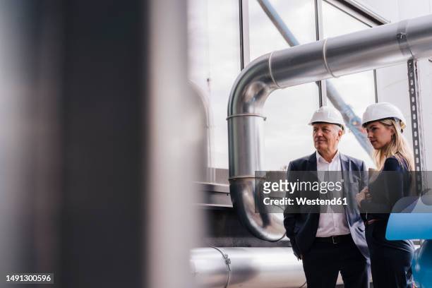businesswoman and senior businessman standing under metal pipe in factory - successor stockfoto's en -beelden
