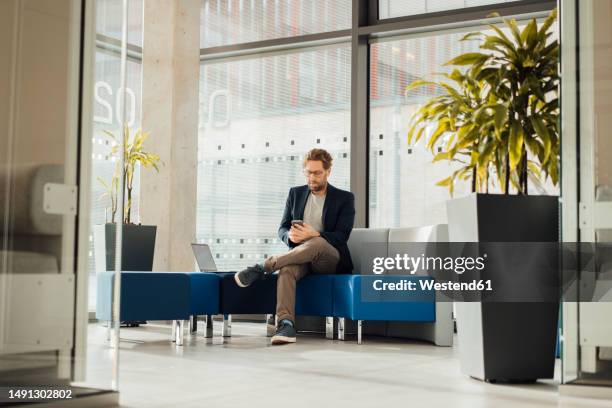 businessman using phone sitting on seat at lobby - business man texting stock pictures, royalty-free photos & images