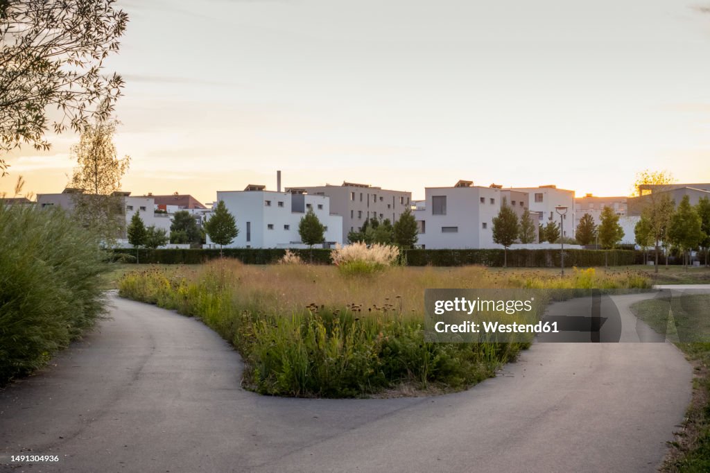Germany, Bavaria, Augsburg, Forking footpath at sunset with suburban houses in background