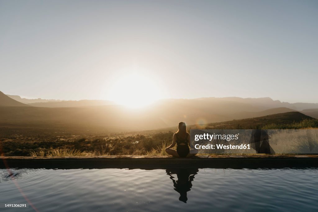 Woman doing yoga sitting by pool at sunset