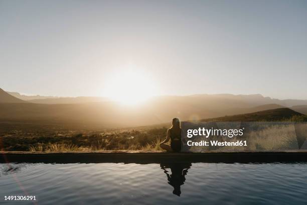 woman doing yoga sitting by pool at sunset - lotus position stock pictures, royalty-free photos & images