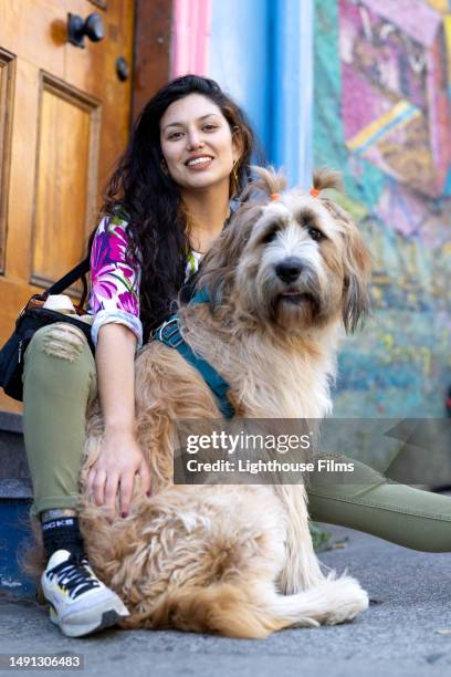 stunning fashionable young woman sits in front of colorful wall to pose with her adorable dog - chili woman photos et images de collection