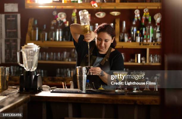 concentrated female bartender pours liquor into shaker while making mixed drinks at dimly lit bar in chile - barman tequila stock pictures, royalty-free photos & images