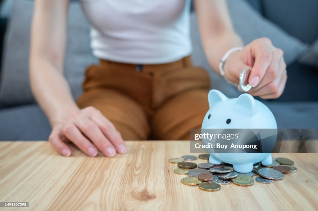 Woman hand while putting a coin into piggy bank for saving money.