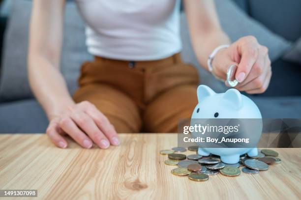 woman hand while putting a coin into piggy bank for saving money. - savings stock pictures, royalty-free photos & images