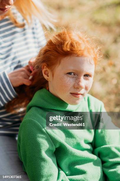 mother braiding hair of daughter outdoors - redhead mom stock pictures, royalty-free photos & images