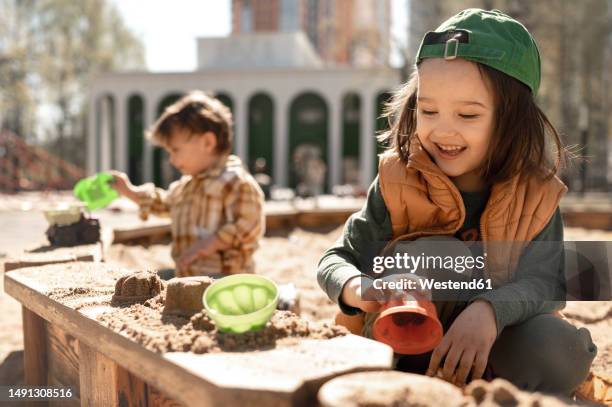 smiling boy playing with sand on playground on sunny day - sandlåda bildbanksfoton och bilder